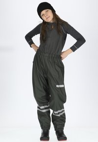 Mørkeblå vandtætte overalls med elastisk talje og reflekterende striber. Kombineret med en grå langærmet top og sort hat. Sorte støvler synlige.