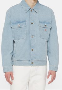 Ljusblå denimjacka med långa ärmar, två framfickor, silverfärgad knappstängning och en broderad logotyp på vänster bröstficka.