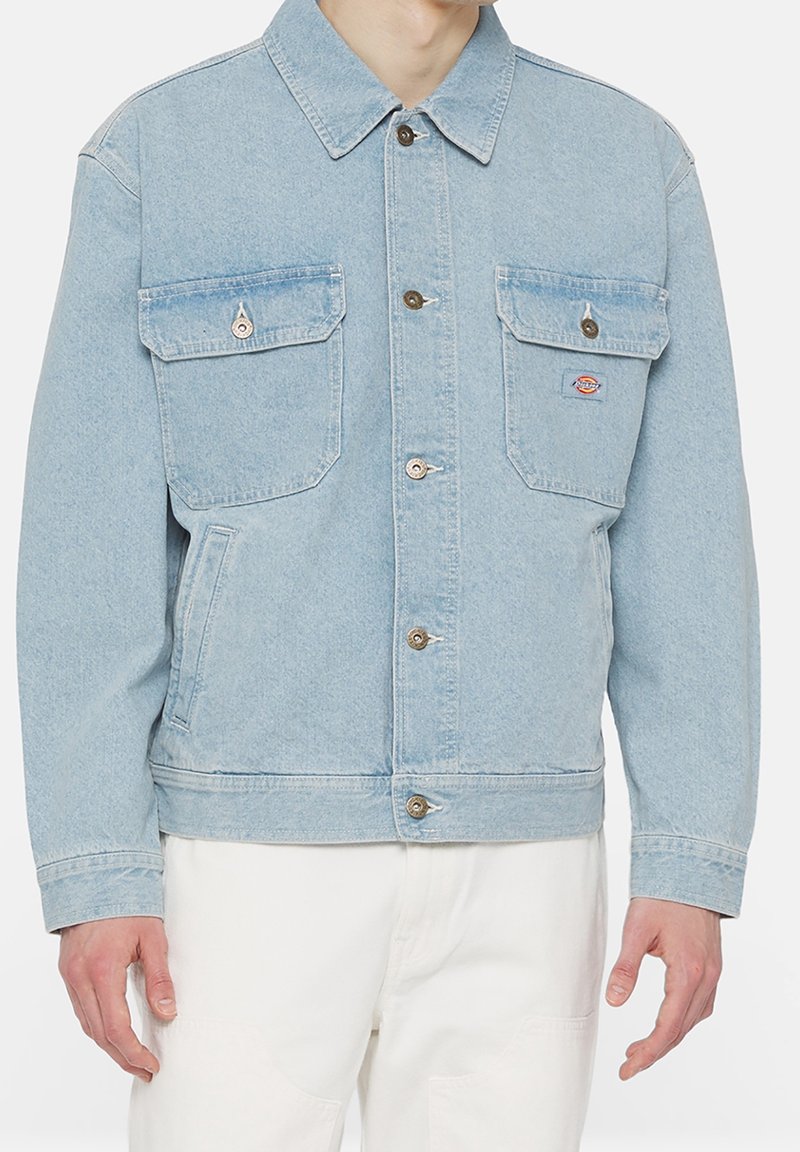 Ljusblå denimjacka med långa ärmar, två framfickor, silverfärgad knappstängning och en broderad logotyp på vänster bröstficka.