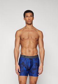 Boxer-briefs bleus à motif avec un design ajusté, fabriqués en matière extensible, dotés d'une ceinture de marque noire.