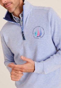 Lichtblauwe pullover met kwart ritssluiting, gemaakt van zacht materiaal, met een logo van zeilboten en een contrasterende binnenkraag in een gedessineerd ontwerp.