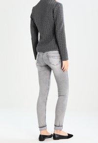 Szary sweter o teksturze, z długimi rękawami, zestawiony z jasnoszarymi obcisłymi dżinsami i czarnymi płaskimi butami. Skupienie na dopasowanym kroju i kontrastach kolorystycznych.