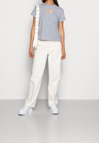 Henkilö, jolla on harmaa Levi's-t-paita, valkoiset leveälahkeiset housut, valkoiset plateausneuleet ja kantaa valkoista olkalaukkua, jossa on niittejä.