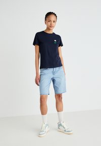 T-shirt de algodão azul-marinho com uma pequena flor bordada no peito, combinada com calções de ganga claros e ténis de cano alto.