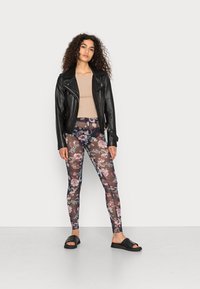 Leggings com padrão floral de textura transparente, apresentando tons de roxo, rosa e azul. Combinados com uma camisola justa bege e uma jaqueta de couro preta.