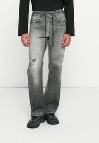 Γκρι τζιν παντελόνια από τζιν ύφασμα με ξεθωριασμένο πλύσιμο. Διαθέτουν φθαρμένες λεπτομέρειες, κανονικές τσέπες και κλείσιμο με κορδόνι στη μέση. Συνδυασμένα με μαύρα παπούτσια.