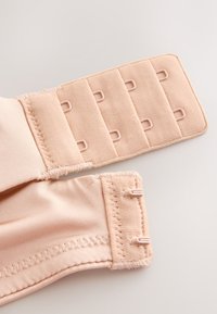Bretelle de soutien-gorge beige extensible avec quatre rangées de fermetures à crochets, posée à plat sur une surface claire.