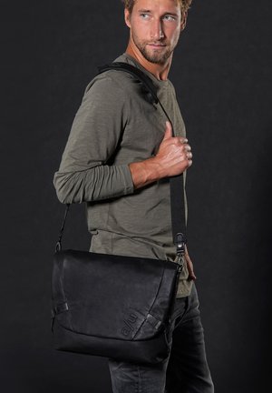 Schwarze Leder-Umhängetasche mit Klappverschluss, verstellbarem Riemen und geprägtem Logo. Glatte Textur mit minimalen Metallakzenten.