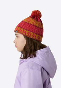 Strikket lue i livlig rosa og oransje, med dusk på toppen, geometriske mønstre og en logomerke. Myk tekstur, tettsittende passform.