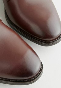 Chaussures en cuir marron avec une finition lisse, bout légèrement pointu et coutures visibles le long du bord de la semelle.