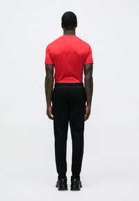 Piros pamut póló fekete tréningnadrággal párosítva. A tréningnadrág gumis derékpánttal és szegélyezett bokarészlel rendelkezik. A lábbelik fekete sportcipők.