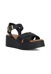 Zwarte gevlochten sandalen met een platformzool en verstelbare gesp. Heeft een bovenkant van synthetisch leer en een tan gekleurde voetbed voor comfort.