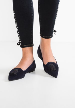 Marineblå ruskindsballerinaer med spids tå og en dekorativ frynse på forfoddet, parret med sorte skinny jeans udsmykket med nagler.