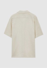 Chemise beige à manches courtes avec tissu texturé, col plat et ourlet droit, vue de dos sur fond clair.