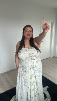Bela cvetna maksi obleka z zelenimi listnatimi vzorci, brez naramnic, tekoča tkanina in z nabranim pasom, ki jo nosi oseba z dolgimi lasmi.