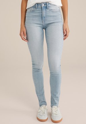 Ljusblå högmidjade jeans har en slim fit, blekt tvätt och subtila slitningar, kombinerade med ljusgrå sneakers och vita snören.
