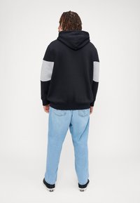Zwarte sweatshirt met capuchon, grijze mouwaccenten en ribgebreide manchetten, gecombineerd met lichtblauwe losvallende jeans en zwarte sneakers.