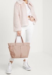 Poskipunan vaaleanpunainen kantolaukku, jossa on kaksi etutaskua ja jämäkkä muotoilu, valmistettu pehmeästä materiaalista. Yhdistetty tekoturkistakin ja valkoisten farkkujen kanssa.