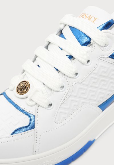 Λευκά και μπλε αθλητικά παπούτσια Versace με ανάγλυφο γεωμετρικό σχέδιο, λευκά κορδόνια και χρυσό έμβλημα Medusa κοντά στην κάτω τρύπα για κορδόνι.