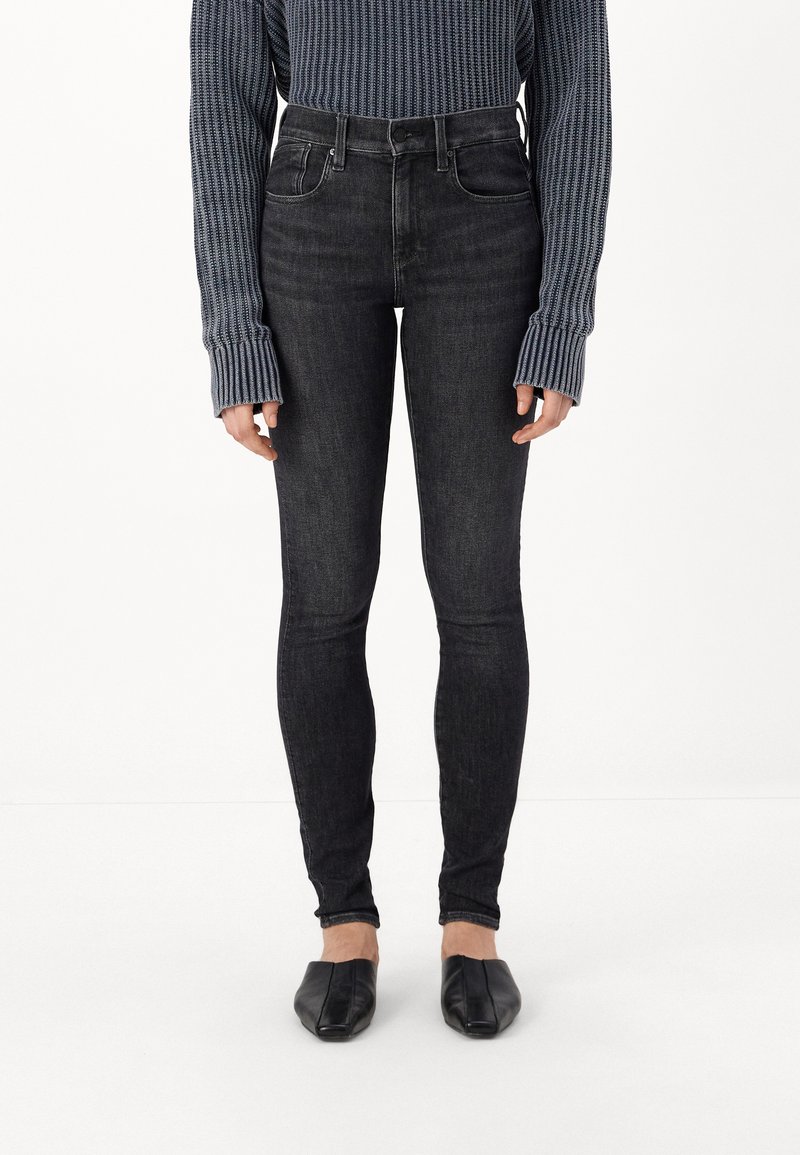 Fekete, skinny farmernadrág, magas derekú fazonnal, enyhén textúrált denim anyagból, párosítva egy bordázott sötétkéks pulóverrel és fekete lapos cipővel.