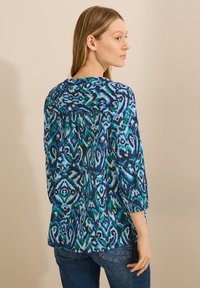Multikleurige top met een patroon in blauwe en groene tinten, met een ronde halslijn, driekwartmouwen en een losse pasvorm met een rugplooi.