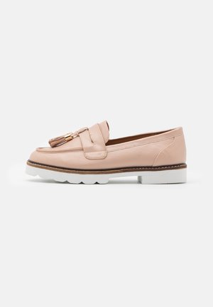 Mocassins en cuir rose clair avec un accent pompon, forme arrondie, semelle en caoutchouc blanche et coutures détaillées le long du bord.