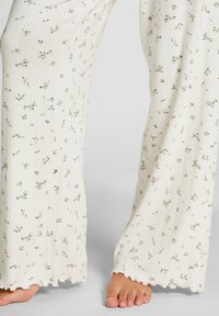 Bloemenpyjamabroek van zacht, textuurwit stof met groene bloemenpatronen. Heeft een uitlopende pijp en een gegolfde zoomafwerking.