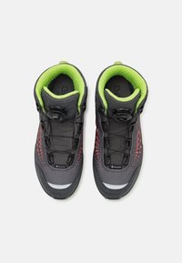 Scarpe da trekking nere e grigie con colletto verde. Presentano una tomaia testurizzata, accenti rossi e un sistema di lacci a rotella per una vestibilità sicura.
