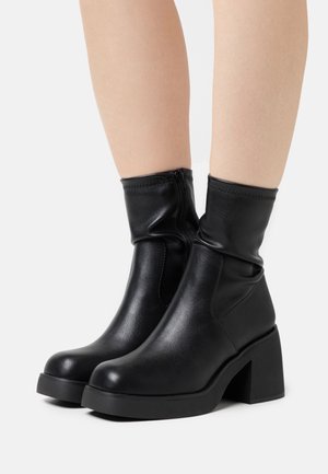 Czarne skórzane botki na kostkę z luźnym fasonem, blokowym obcasem, zamek błyskawiczny oraz gładką teksturą.