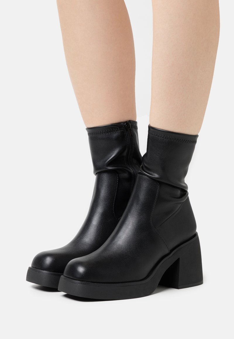 Černé kožené kotníkové boty s uvolněným designem, blokovým podpatkem, zipovým uzavíráním a hladkým povrchem.