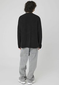 Pull en maille noire avec texture côtelée, col rond et manches longues. Assorti à un pantalon ample gris clair et des baskets blanches.