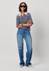 Gestreepte polo met een witte kraag, versierde schouders, in combinatie met lichtblauwe jeans en zilveren puntige schoenen, gedragen met donkere zonnebril.