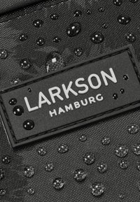 Tessuto nero testurizzato con gocce d'acqua, adornato da un'etichetta rettangolare con la scritta "LARKSON HAMBURG" in caratteri bianchi in grassetto.