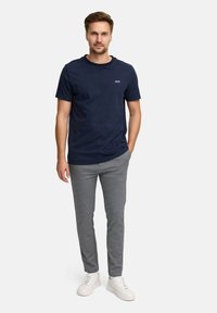 Marine bomull t-skjorte med rund hals og liten hvit "JEFF" logo, parret med lysegrå slim-fit bukser og hvite joggesko på en ensfarget bakgrunn.