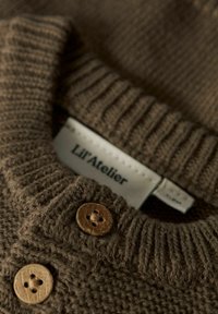 Gros plan d'un pull en tricot marron avec des boutons ronds en bois et une étiquette "Lil' Atelier" à l'intérieur du col.