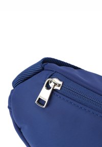 Mörkblå nylonväska med slät textur, prydd med en silverdragkedjehandtag märkt "BOGNER" och förstärkt sömnad längs kanterna.