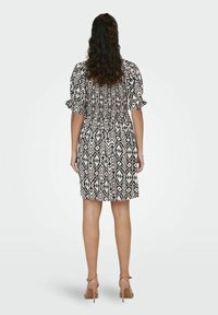 Vestido de estampado negro y crema con mangas abullonadas y cintura elástica. Llega por encima de la rodilla y tiene una textura suave. Se lleva con tacones nude.