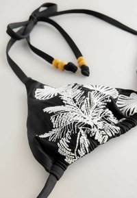 Sort bikinitop med hvid blad broderi, justerbare stropper med sorte og gule perler, samt en rynket midte for en tætsiddende pasform.