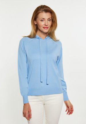 Felpa leggera azzurra con coulisse, polsini e orlo a coste; texture morbida, vestibilità comoda e maniche raglan; indossata con pantaloni bianchi.