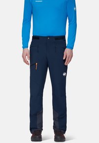 Granatowe spodnie softshell z regulowaną talią, dwoma zamykanymi na zamek kieszeniami, pomarańczowym uchwytem zamka i siateczkowymi akcentami przy mankietach.
