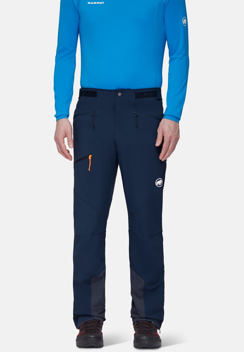 Granatowe spodnie softshell z regulowaną talią, dwoma zamykanymi na zamek kieszeniami, pomarańczowym uchwytem zamka i siateczkowymi akcentami przy mankietach.