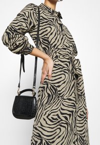 Šaty ve vzoru zebra v béžové a černé barvě, s páskem v oblasti pasu a dlouhými rukávy. Je držená malá černá kabelka s krokodýlím vzorem.