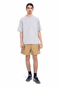 Šedé oversized tričko s krátkými rukávy, khaki šortky, černé ponožky a šedé tenisky. Jednoduchý design bez výrazných vzorů nebo akcentů.
