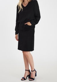 Černý dlouhý rukáv s výstřihem do V a volným střihem, doplněný černou sukní a námořnickými sandály na vysokém podpatku s pásky kolem kotníků.