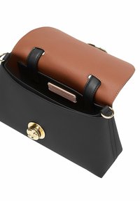 Bolso de mano de cuero negro con una solapa de cuero marrón, herrajes dorados y una forma estructurada. Etiqueta interior visible.