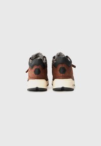Scarpe in pelle marrone con un morbido interno grigio, dettagli neri e una suola robusta bianca e nera, dotate di una piccola linguetta sul retro.