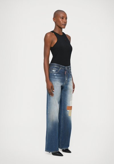 Top negro sin mangas combinado con jeans de pierna ancha azules que presentan parches desgastados y un lavado descolorido, complementado con zapatos negros de punta.