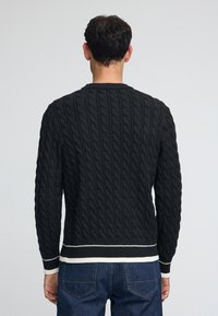 Mörk kabelstickad tröja med ribbad halsringning och ärmslut, kontrasterande vita och svarta ränder i fållen, strukturerat mönster över hela.