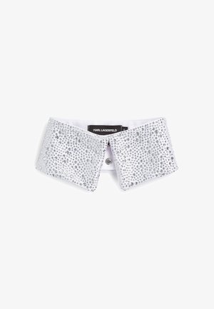 Srebrna ovratnica z nizom rhinestones na belem tekstilnem podlagu, zavezana s centralnim gumbom, namenjena okrasitvi.