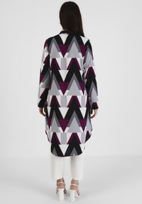 Longue tunique à motif géométrique avec des triangles noirs, blancs, gris et violets. Fabriquée dans un tissu léger avec des manches longues.